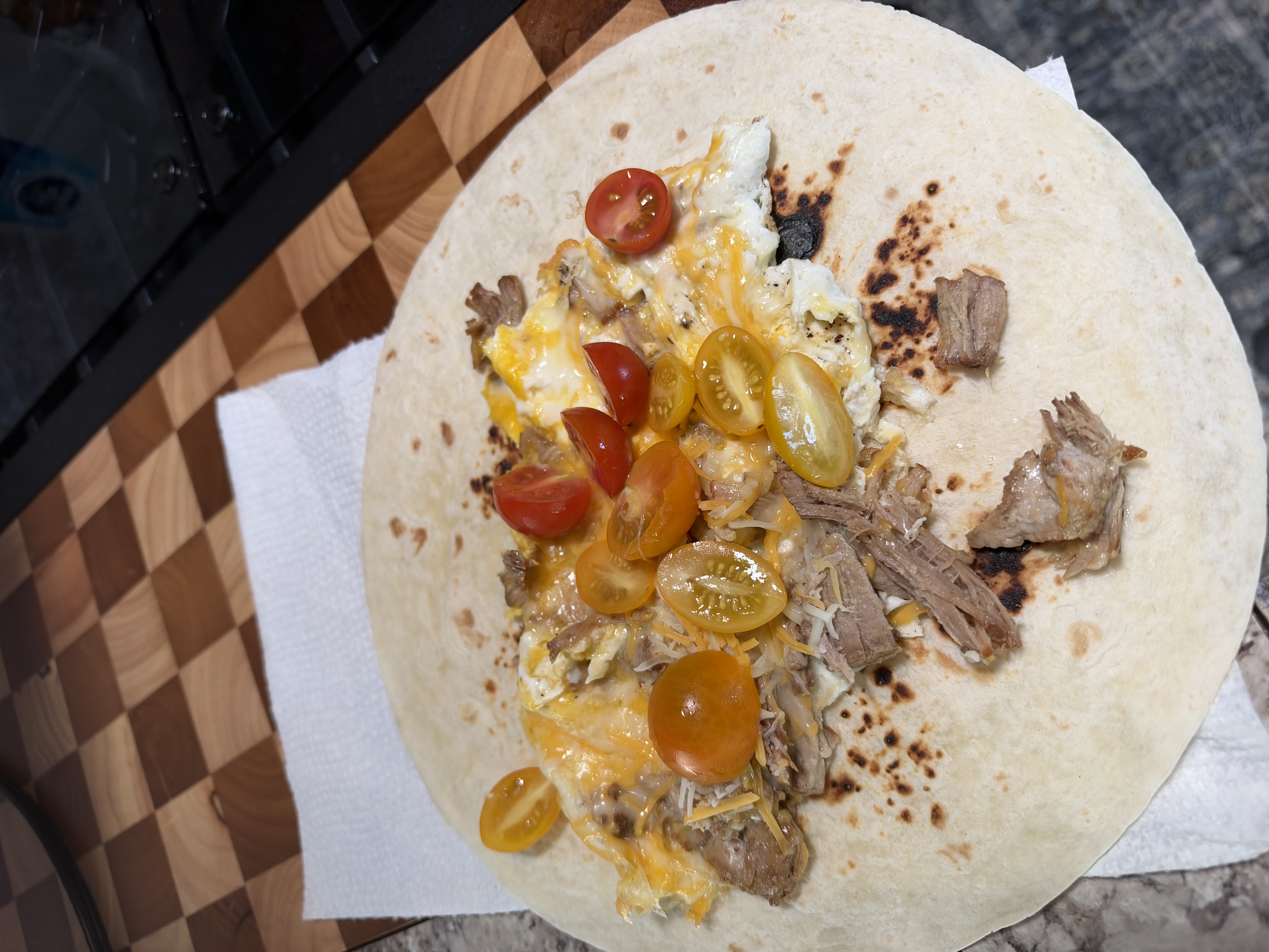 A tortilla topped with eggs, cheese, and tomatoes on a cutting board